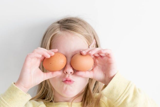 Little Girl holding two eggs playfully in front of her eyes for Easter at ISL