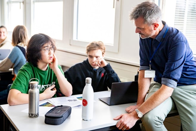 Two students at their desks talking with their teacher at ISL